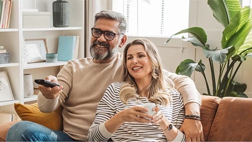 Man and women sitting on sofa with TV remote.